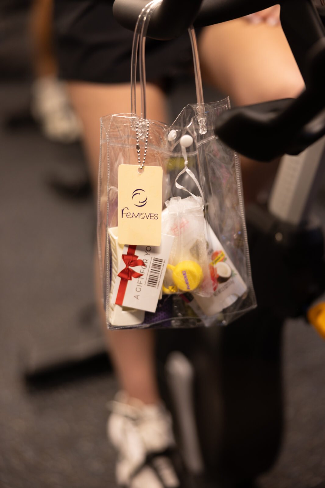 A FeMoves gift bag with a swirl-logo tag hanging from a bike's handlebar