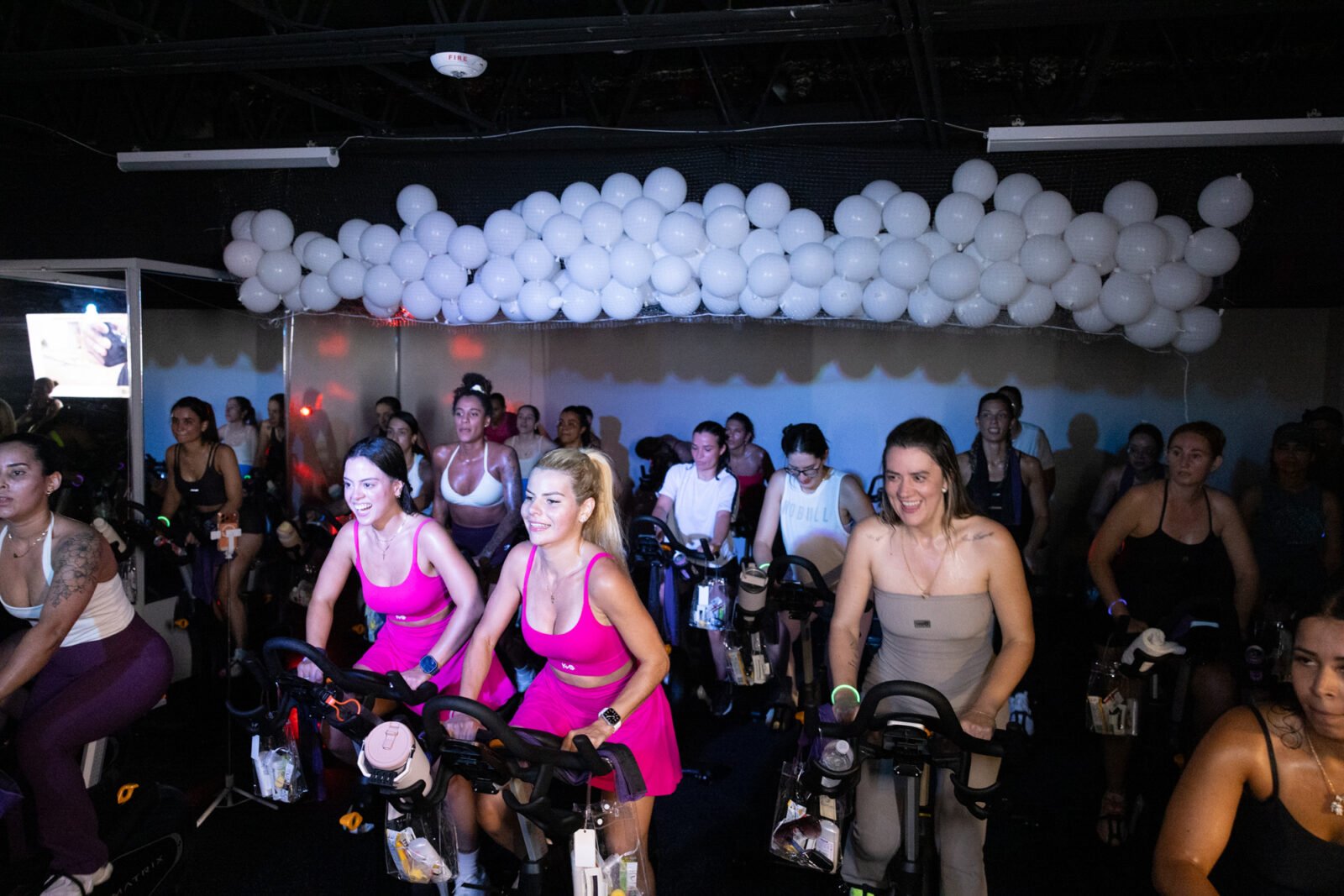 Riders in hot pink pedalling under a ceiling of white balloons