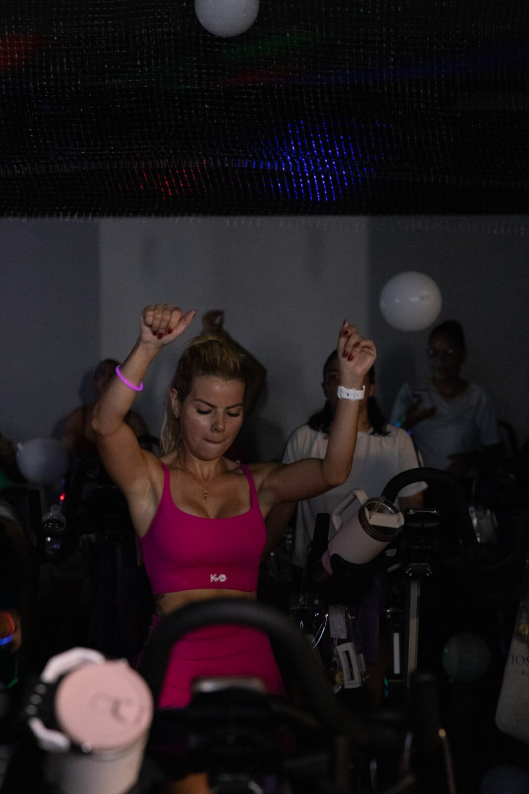 A rider in a hot-pink top dances with both arms raised as balloons fall around her