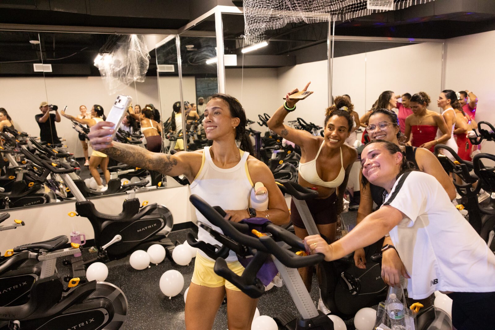 Riders crowd in for a selfie next to the bikes after class, balloons scattered on the floor